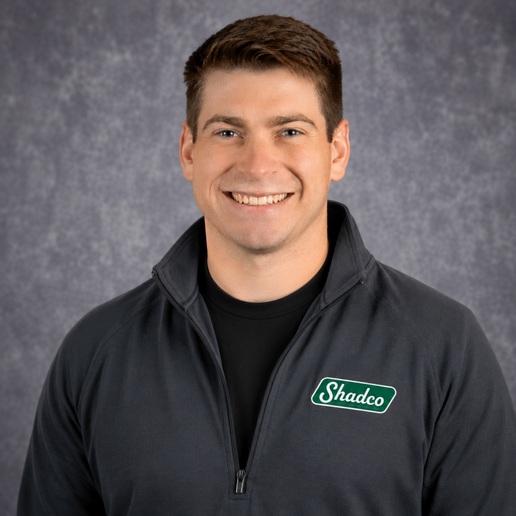 Head-and-shoulders portrait of a smiling man in a dark zip-up jacket with a Shadco logo against a gray backdrop.