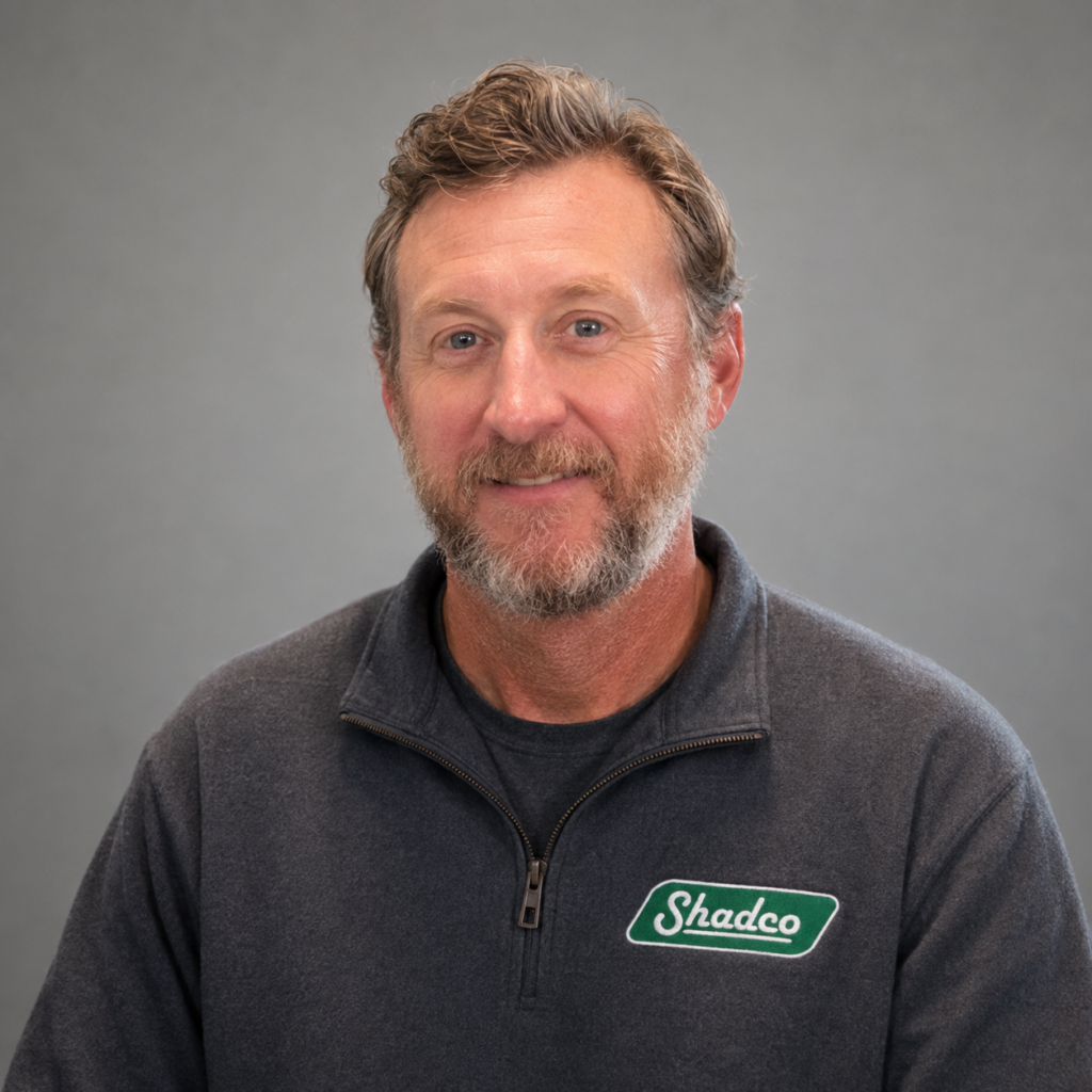 Portrait of a middle-aged man with a gray beard and short light brown hair, wearing a dark zip-up sweater with a ShadeCo logo on the chest.